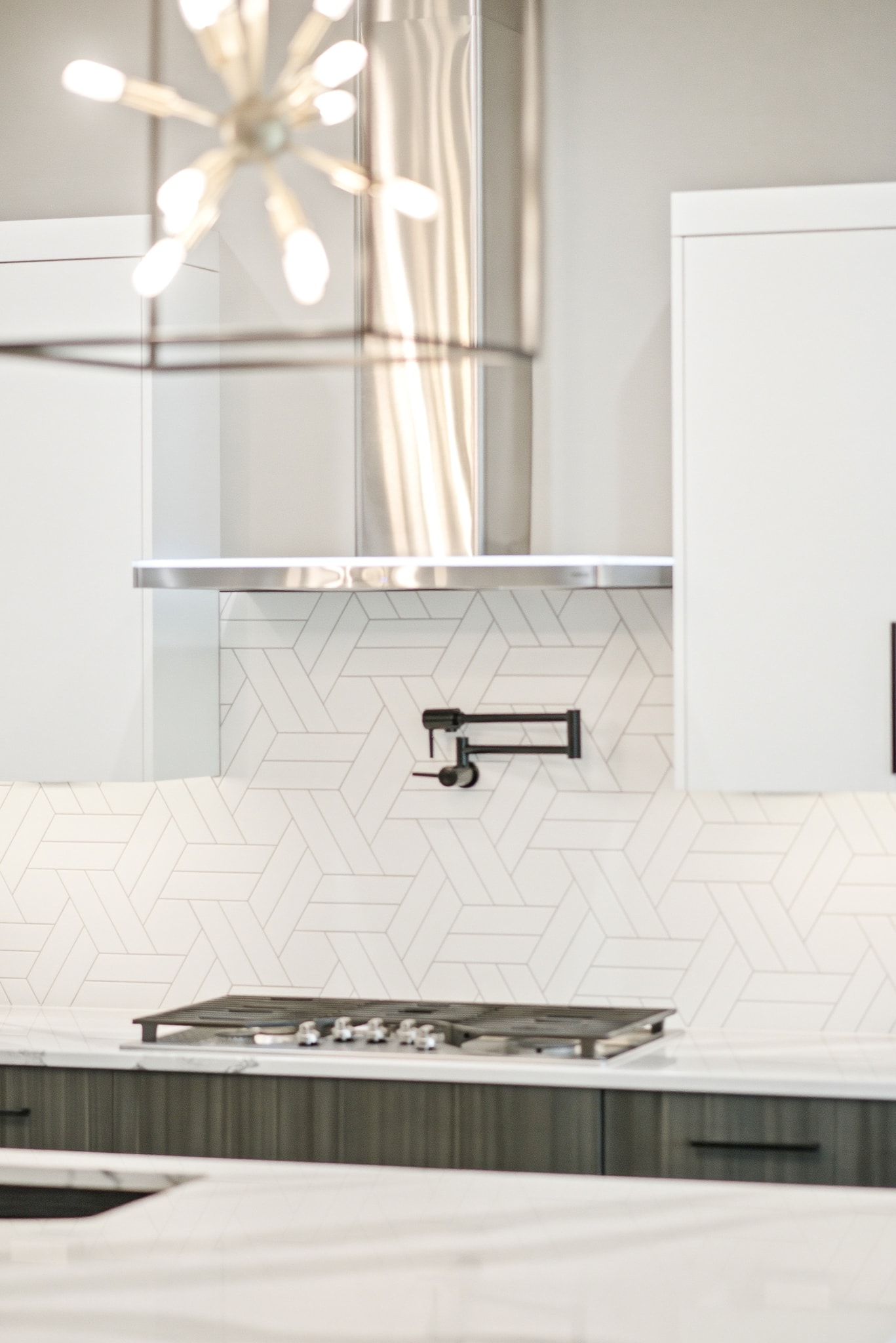 White geometric tile backsplash with sputnik chandelier and stainless range hood